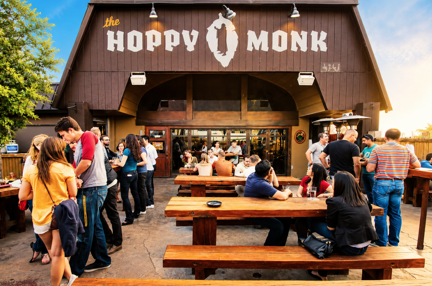 Guests gathered at long picnic tables on the front patio beneath the Hoppy Monk sign.